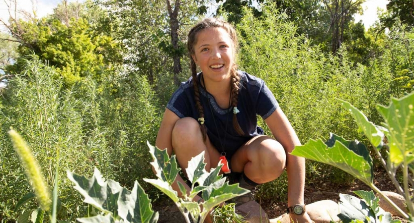 a student who is working in a garden smiles at the camera